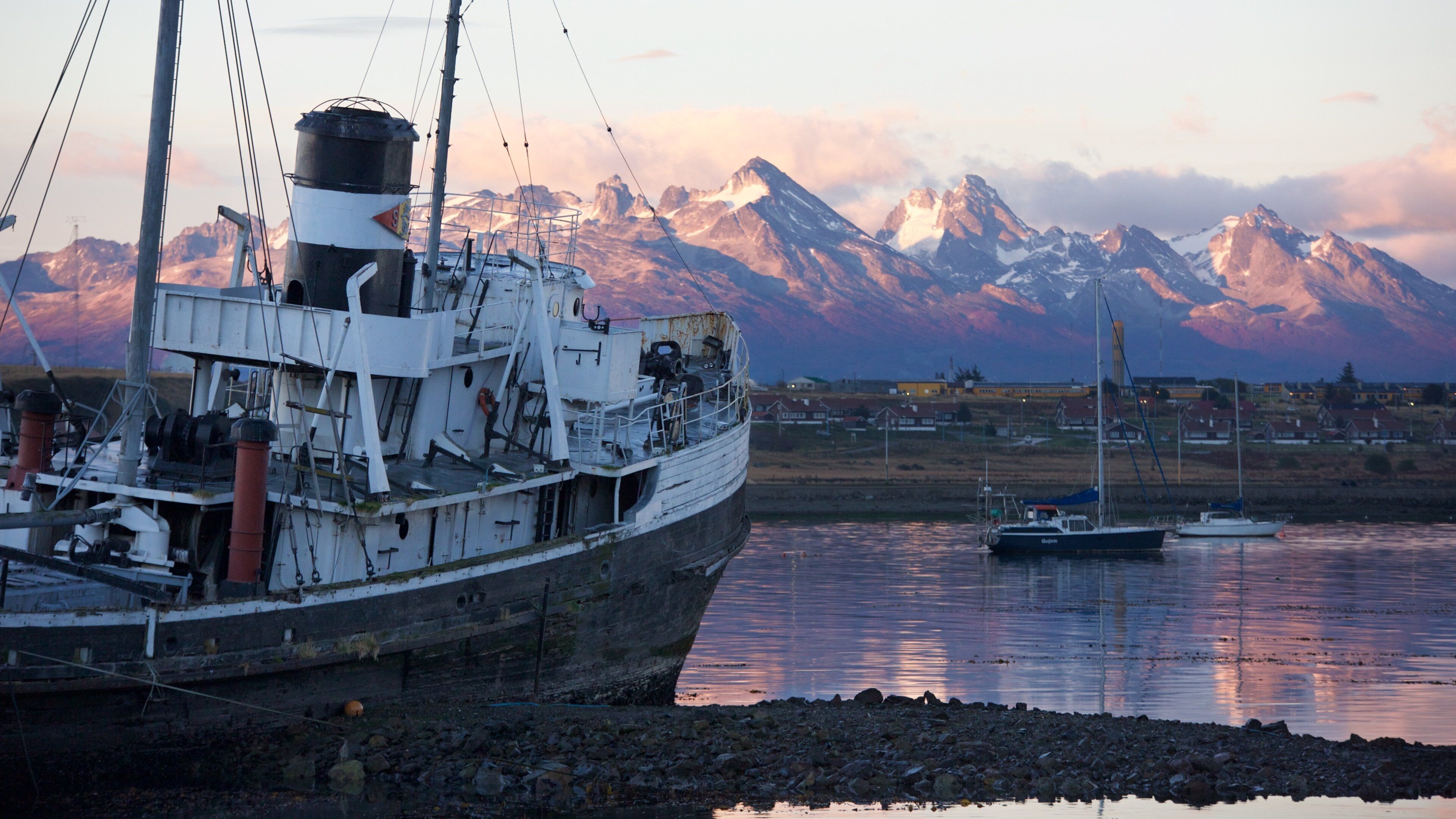 A large ship docked at a harbor with a backdrop of snow-capped mountains.
