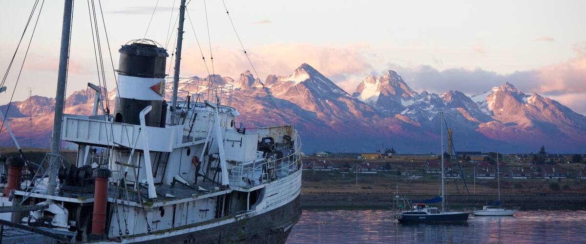 A large ship docked at a harbor with a backdrop of snow-capped mountains.