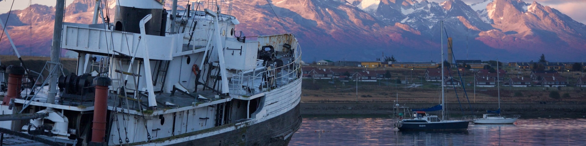 A large ship docked at a harbor with a backdrop of snow-capped mountains.