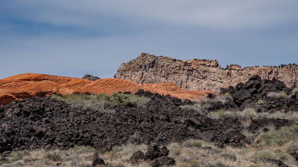 A rugged landscape with red and brown rock formations, sparse vegetation, and a clear sky.