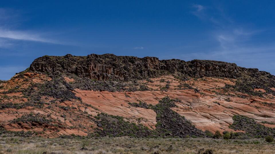 A rugged mountain with reddish rock formations and sparse vegetation.