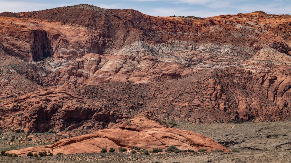 A rugged desert landscape with layered rock formations and sparse vegetation.