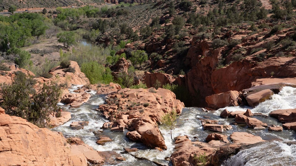 A river flowing through a canyon with red rock formations and distant mountains.