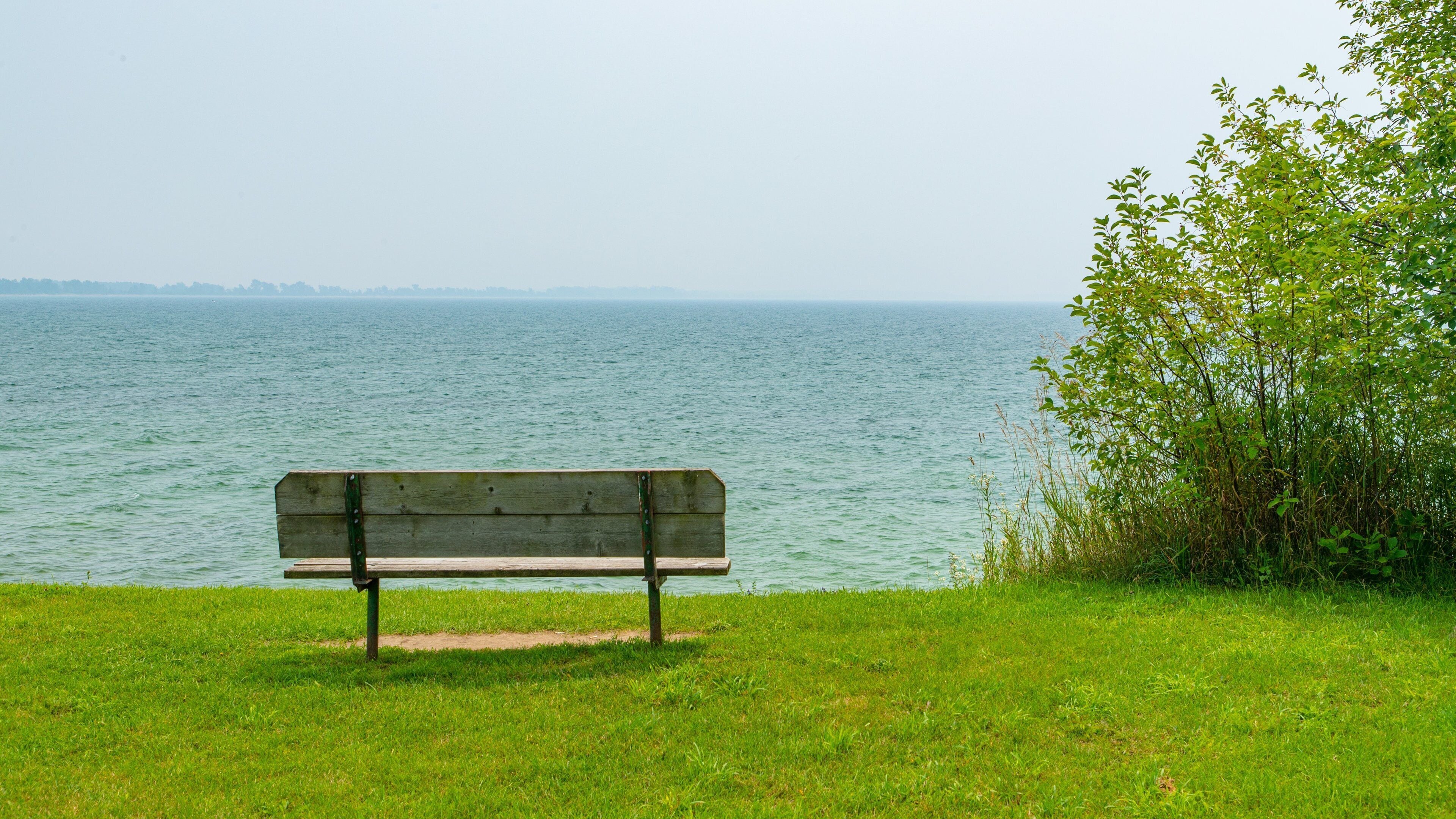A wooden bench on a grassy area overlooking a calm body of water.