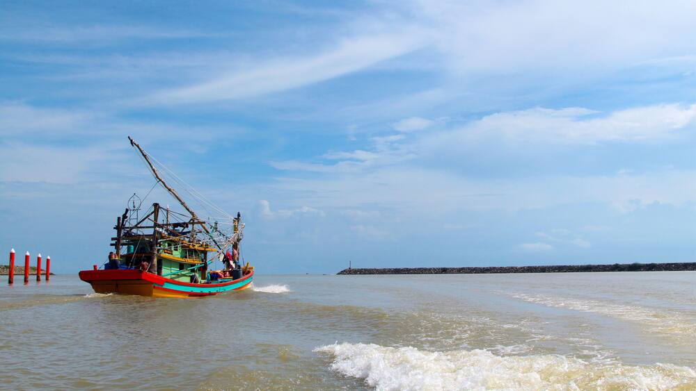 A seascape view of a fisherman fishing boat heading towards an open ocean for fishing over a blue bright sky and a cloudy day. Image shoot from a boat at Kuala Besut Jetty, Terangganu, Malaysia