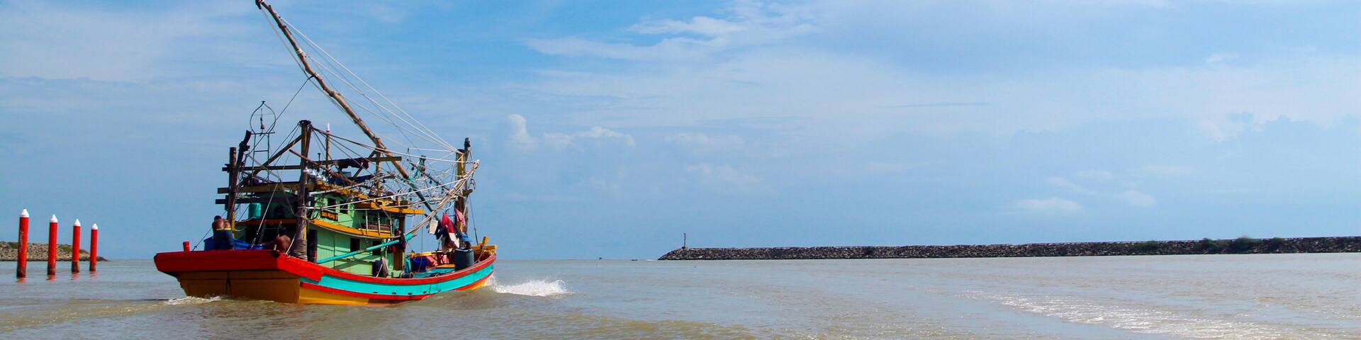 A seascape view of a fisherman fishing boat heading towards an open ocean for fishing over a blue bright sky and a cloudy day. Image shoot from a boat at Kuala Besut Jetty, Terangganu, Malaysia