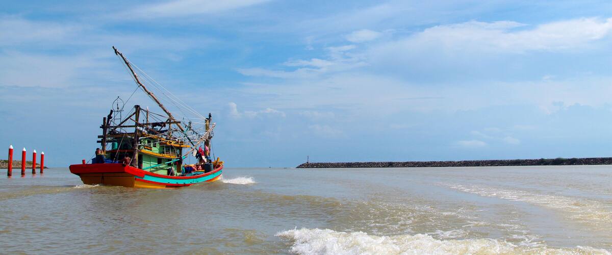 A fishing boat on calm waters with a clear sky and a distant pier.