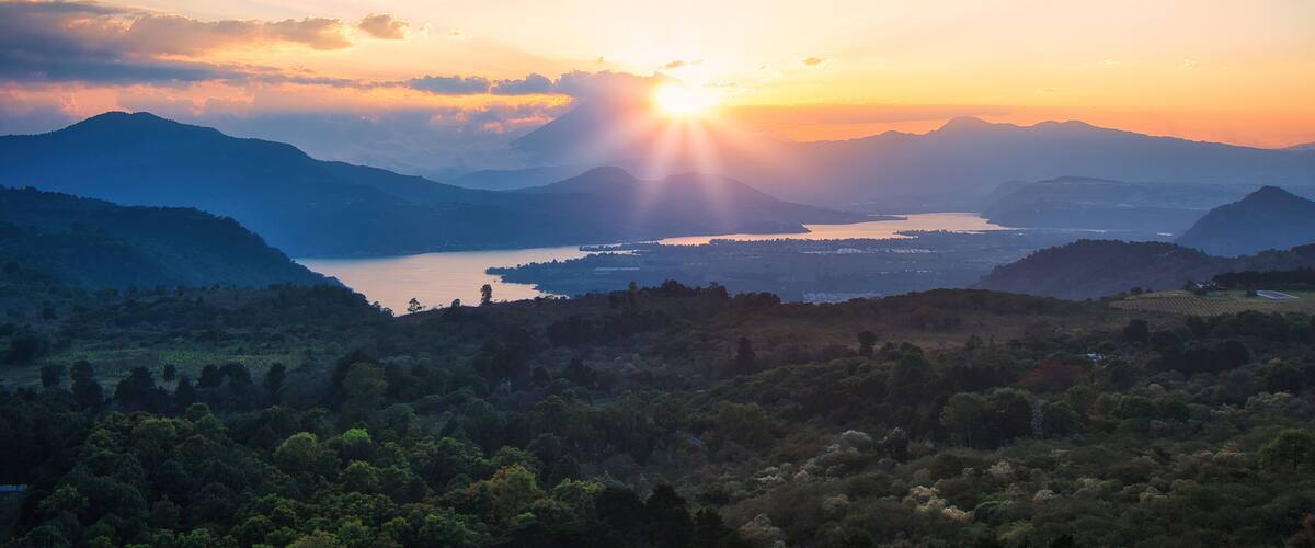 A mountainous landscape with a lake and a sunset.