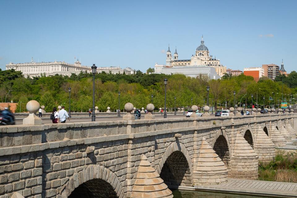 Uma ponte de pedra com arcos, um rio e uma grande catedral ao fundo.