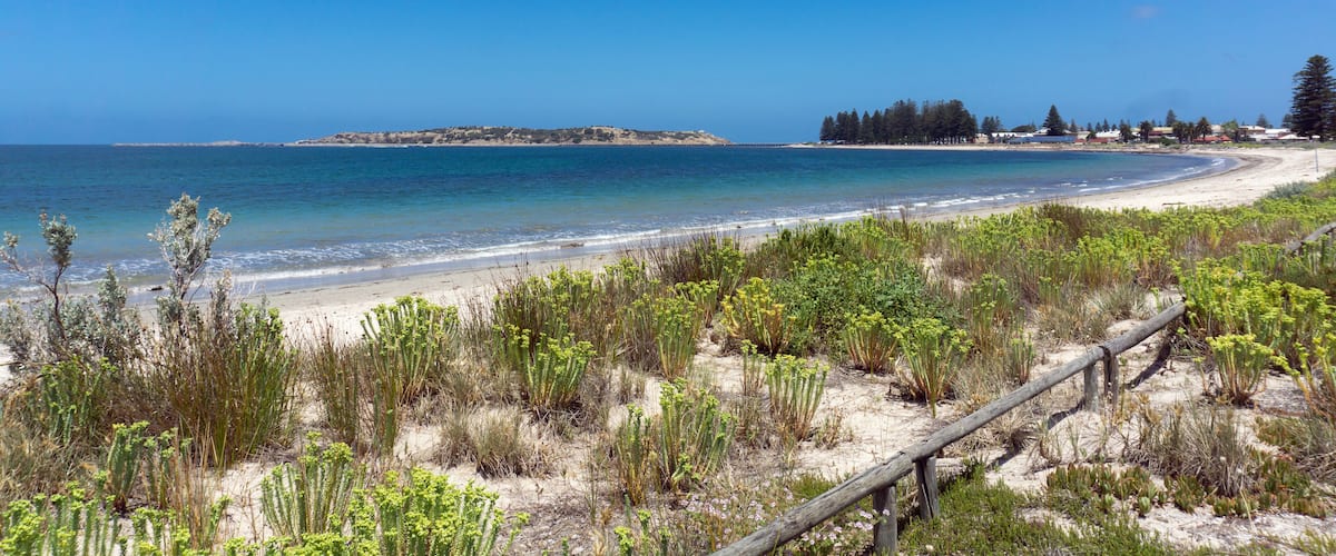 A coastal landscape with a sandy beach, green vegetation, and a clear blue sky.