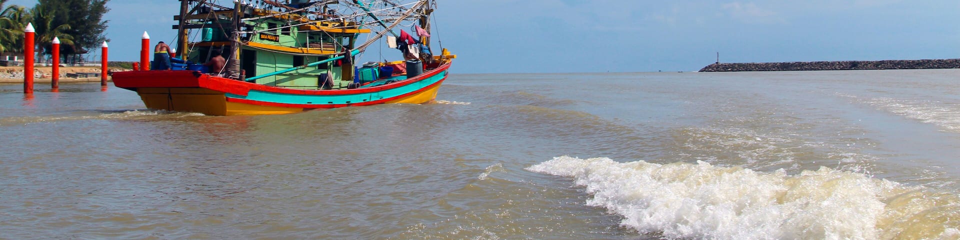 A seascape view of a fisherman fishing boat heading towards an open ocean for fishing over a blue bright sky and a cloudy day. Image shoot from a boat at Kuala Besut Jetty, Terangganu, Malaysia
