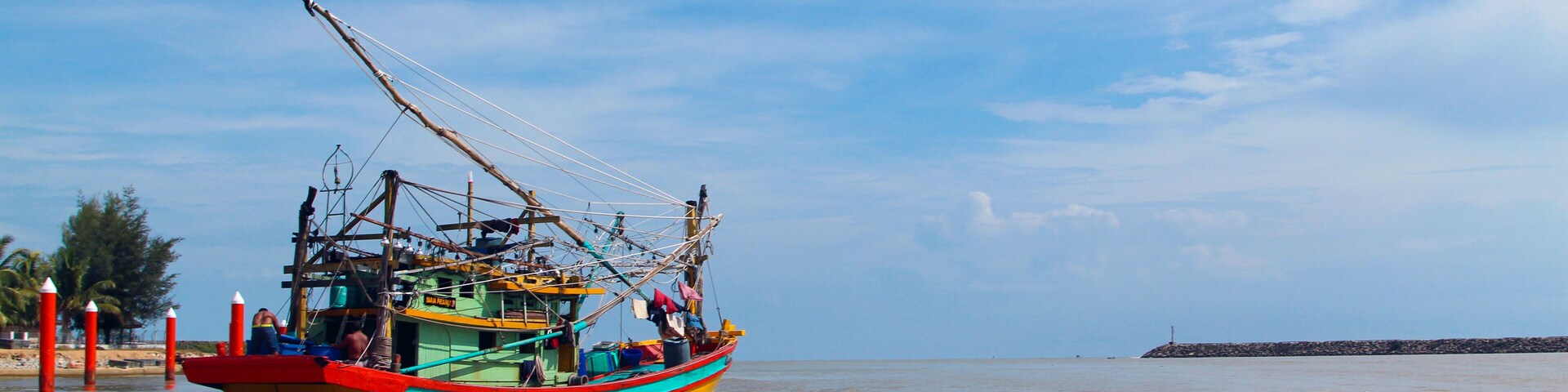 A seascape view of a fisherman fishing boat heading towards an open ocean for fishing over a blue bright sky and a cloudy day. Image shoot from a boat at Kuala Besut Jetty, Terangganu, Malaysia