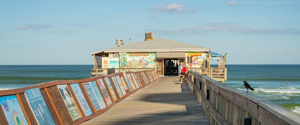 A pier leading to a beachside restaurant with a mural and a signboard.