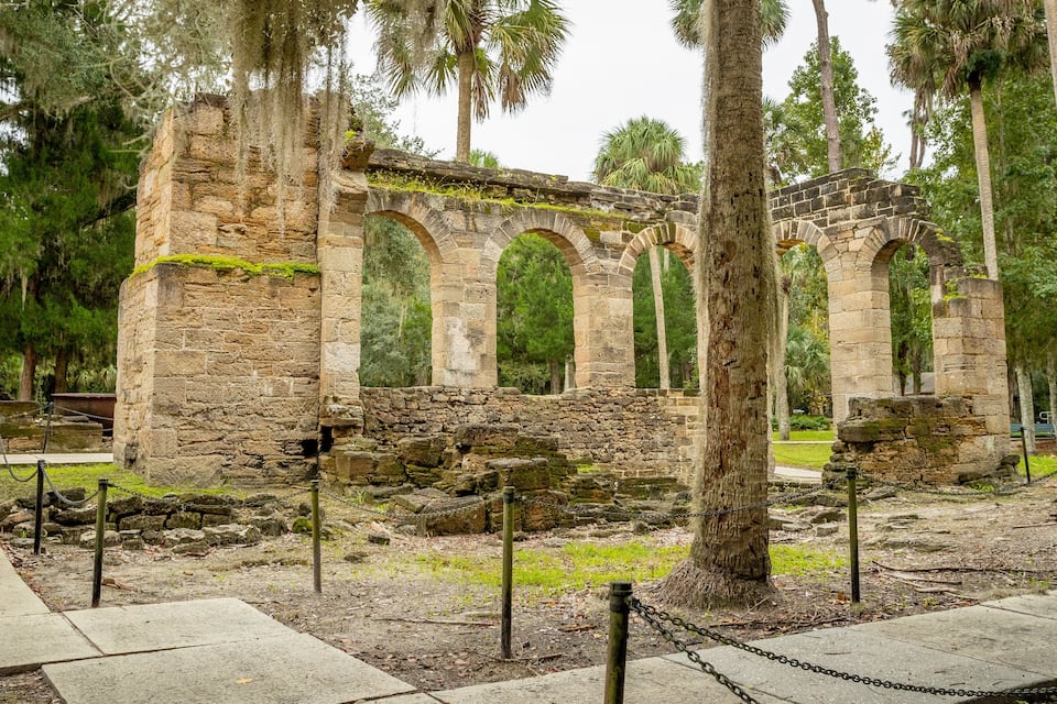 Ancient stone ruins with arches, surrounded by trees and a pathway.