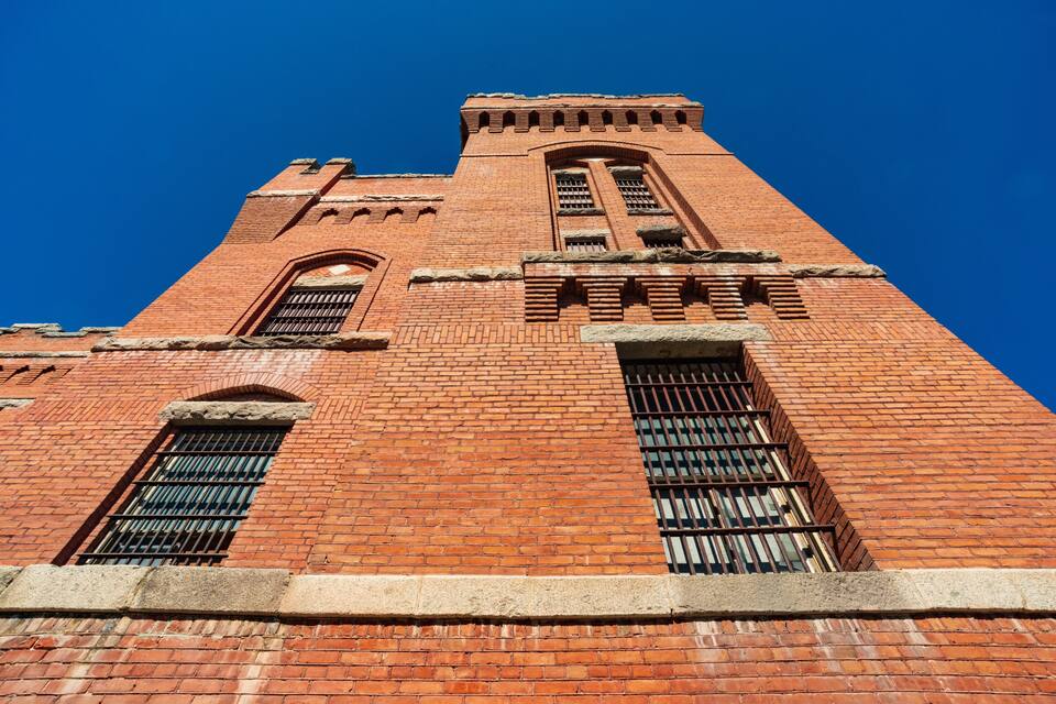 Uma torre de tijolos alta, com janelas em arco e um telhado pontiagudo.