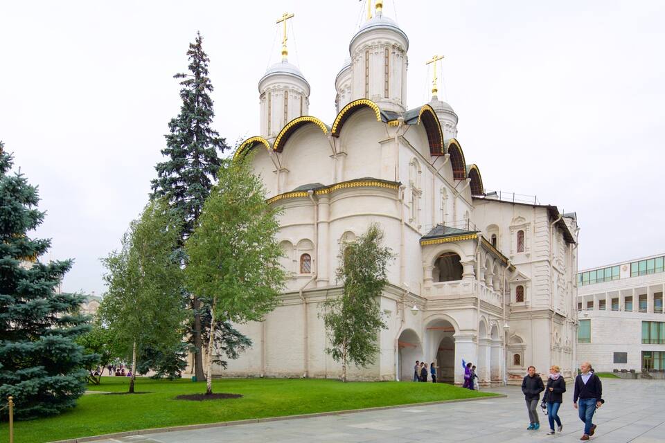 Una iglesia grande de color blanco con cúpulas doradas y cruces, rodeada de árboles y un camino empedrado.