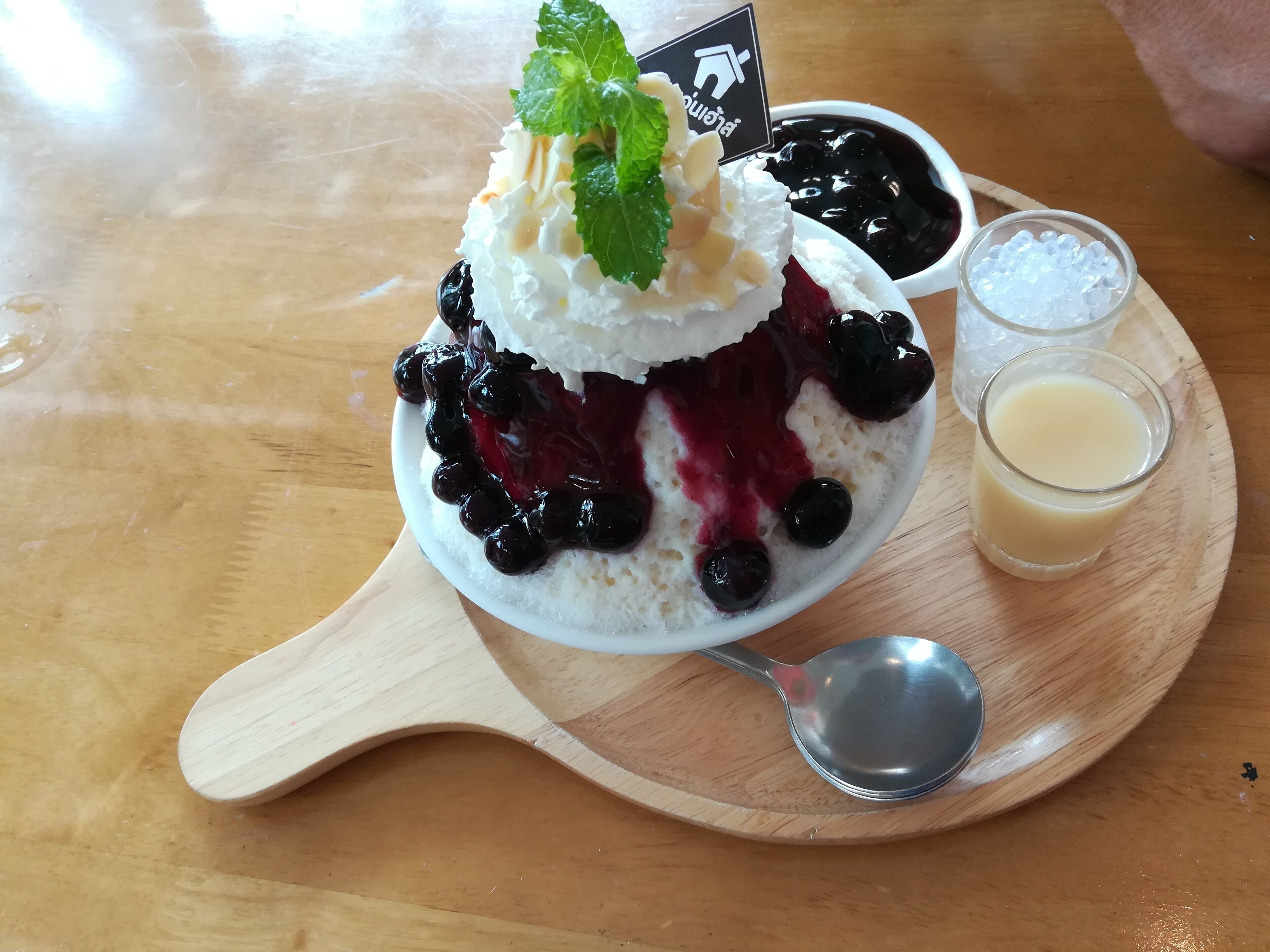 A dessert with whipped cream, blueberries, and a mint garnish on a wooden board.