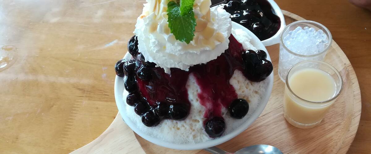 A dessert with whipped cream, blueberries, and a mint garnish on a wooden board.