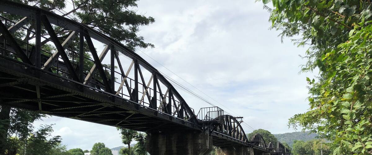 A steel bridge over a river with boats docked at the riverbank.
