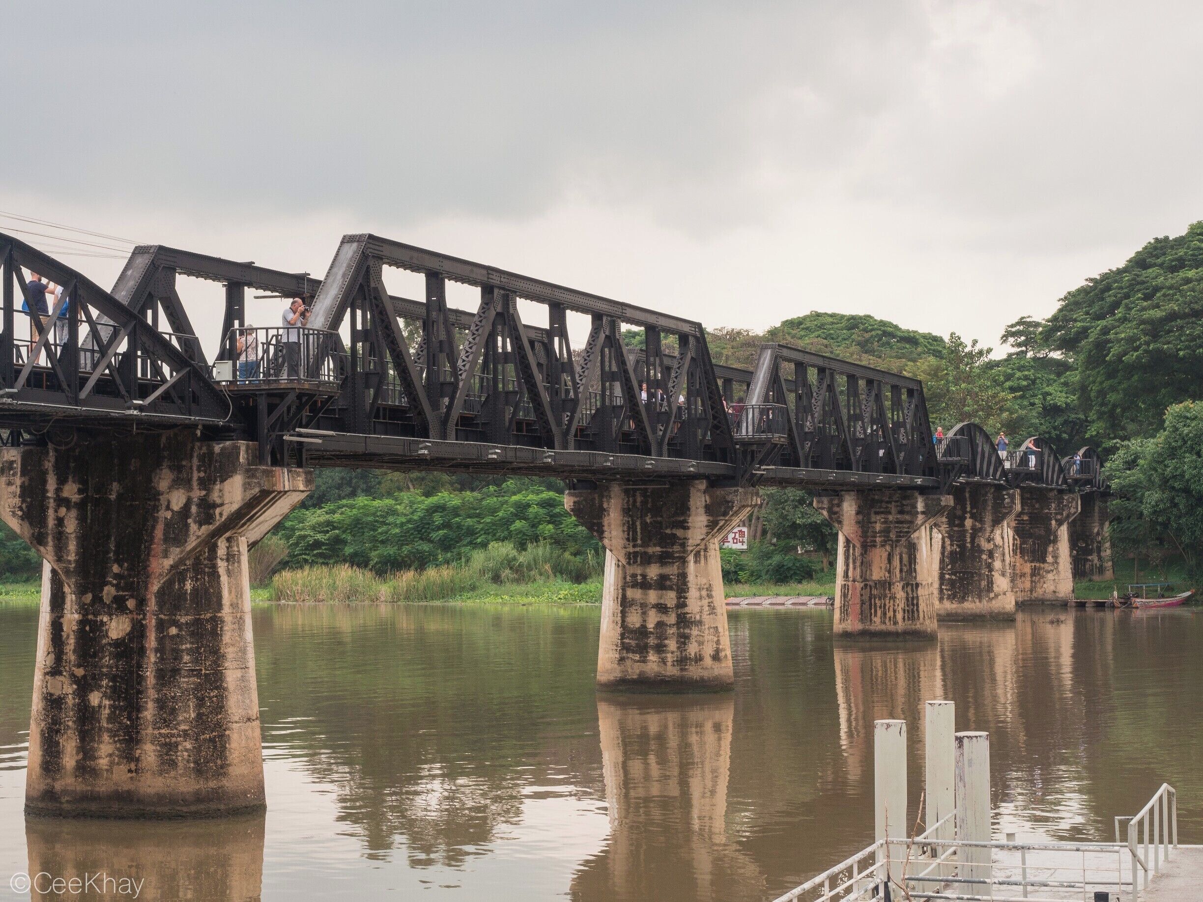 A large, old metal bridge spanning a calm river, with people walking on it.