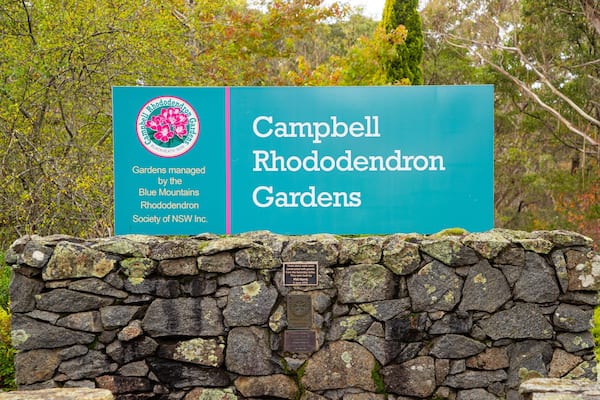 Un panneau indiquant l’entrée des jardins de rhododendrons Campbell, avec un mur de pierres au premier plan.