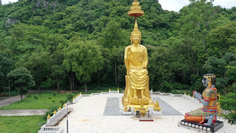 A large golden Buddha statue surrounded by lush greenery and a smaller seated Buddha statue.