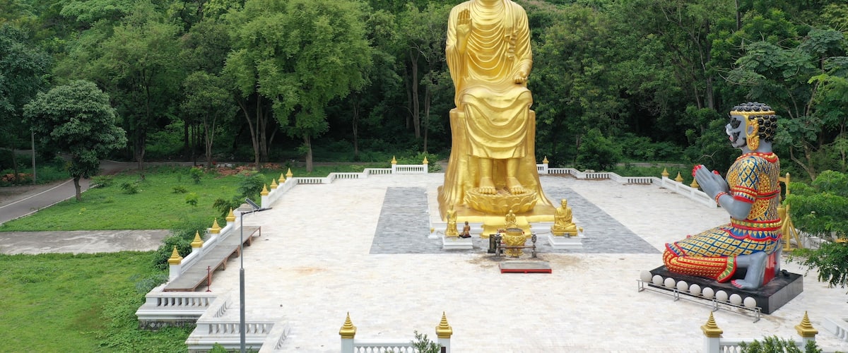 A large golden Buddha statue surrounded by lush greenery and a smaller seated Buddha statue.