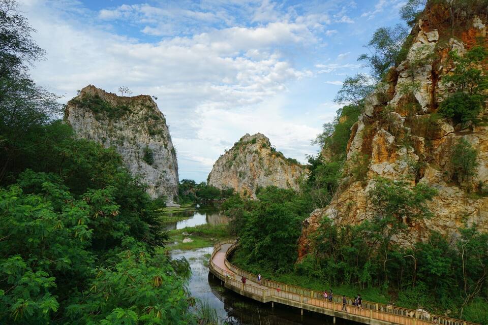 A river winding through a lush valley with rocky cliffs and a wooden bridge.