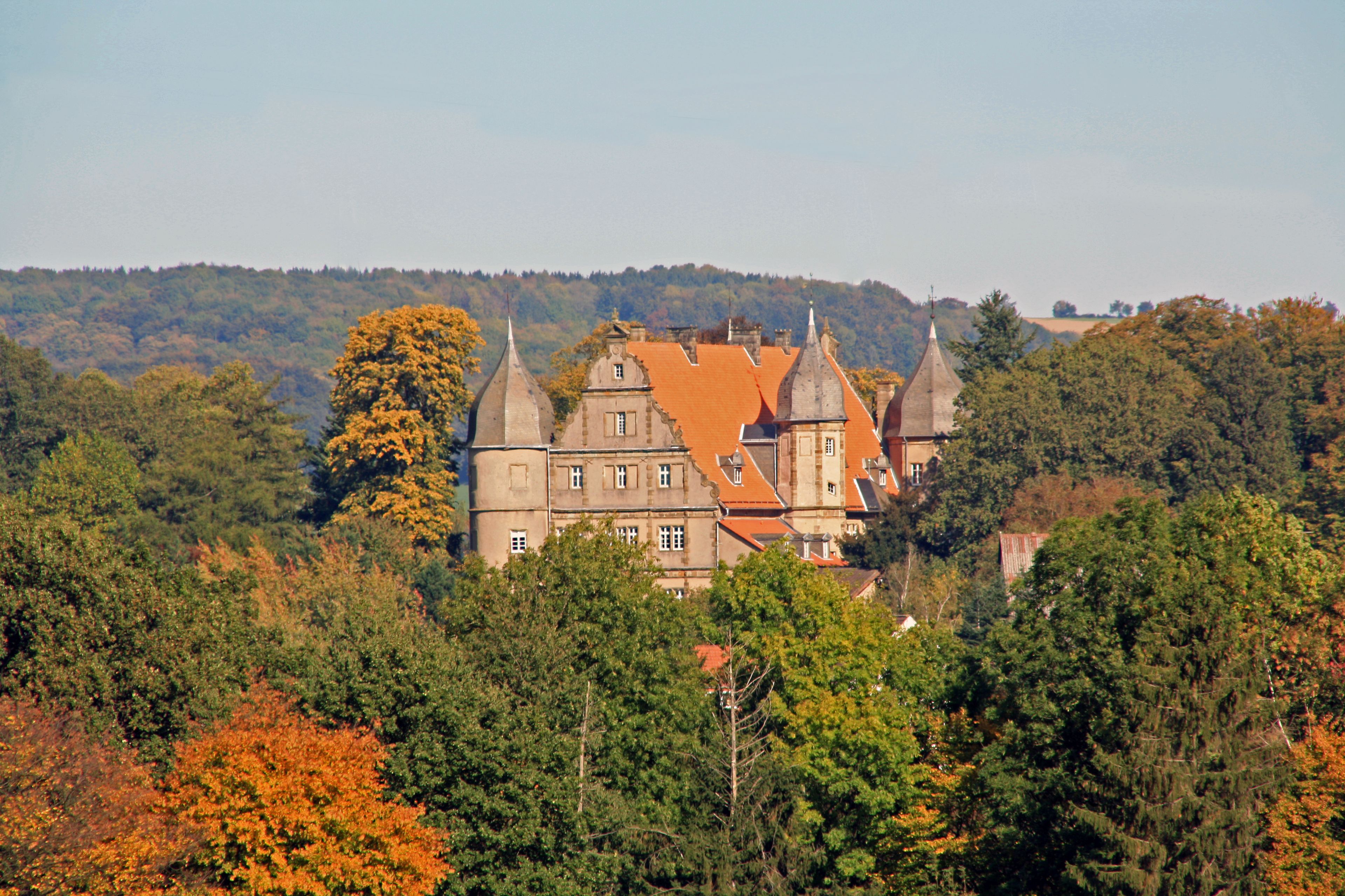 Ein historisches Gebäude mit mehreren Türmen, umgeben von dichtem Wald und Herbstlaub.