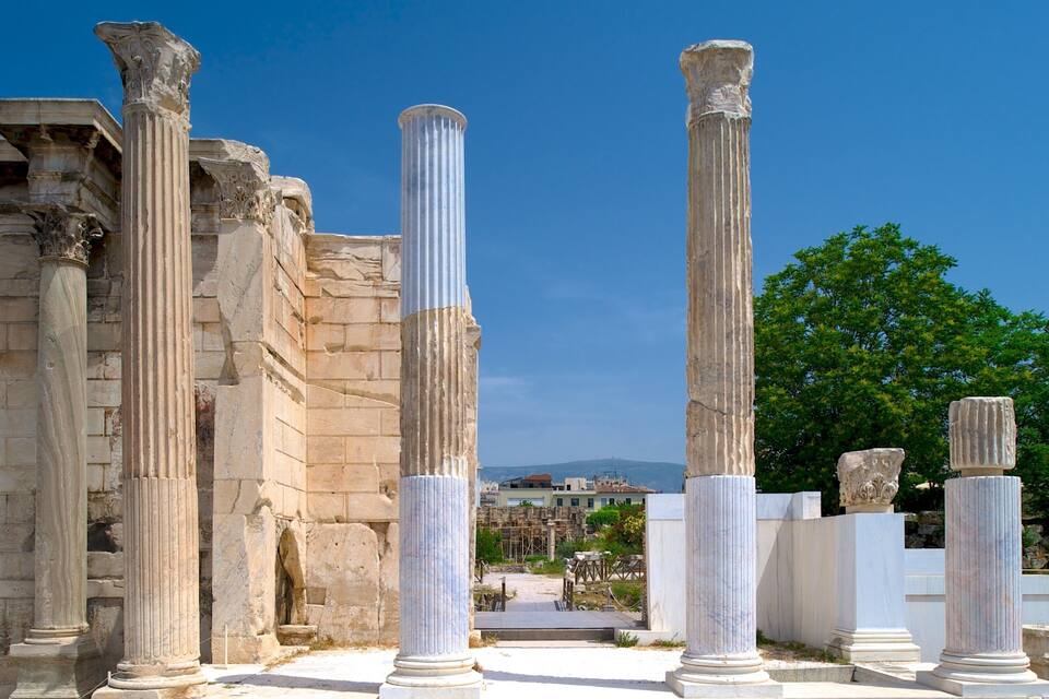 Columnas de piedra antiguas y ruinas bajo un cielo azul claro y montañas distantes.
