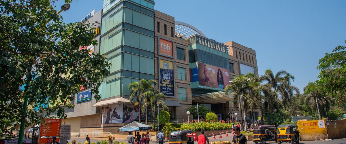 A busy urban street with modern buildings, palm trees, and various shops.