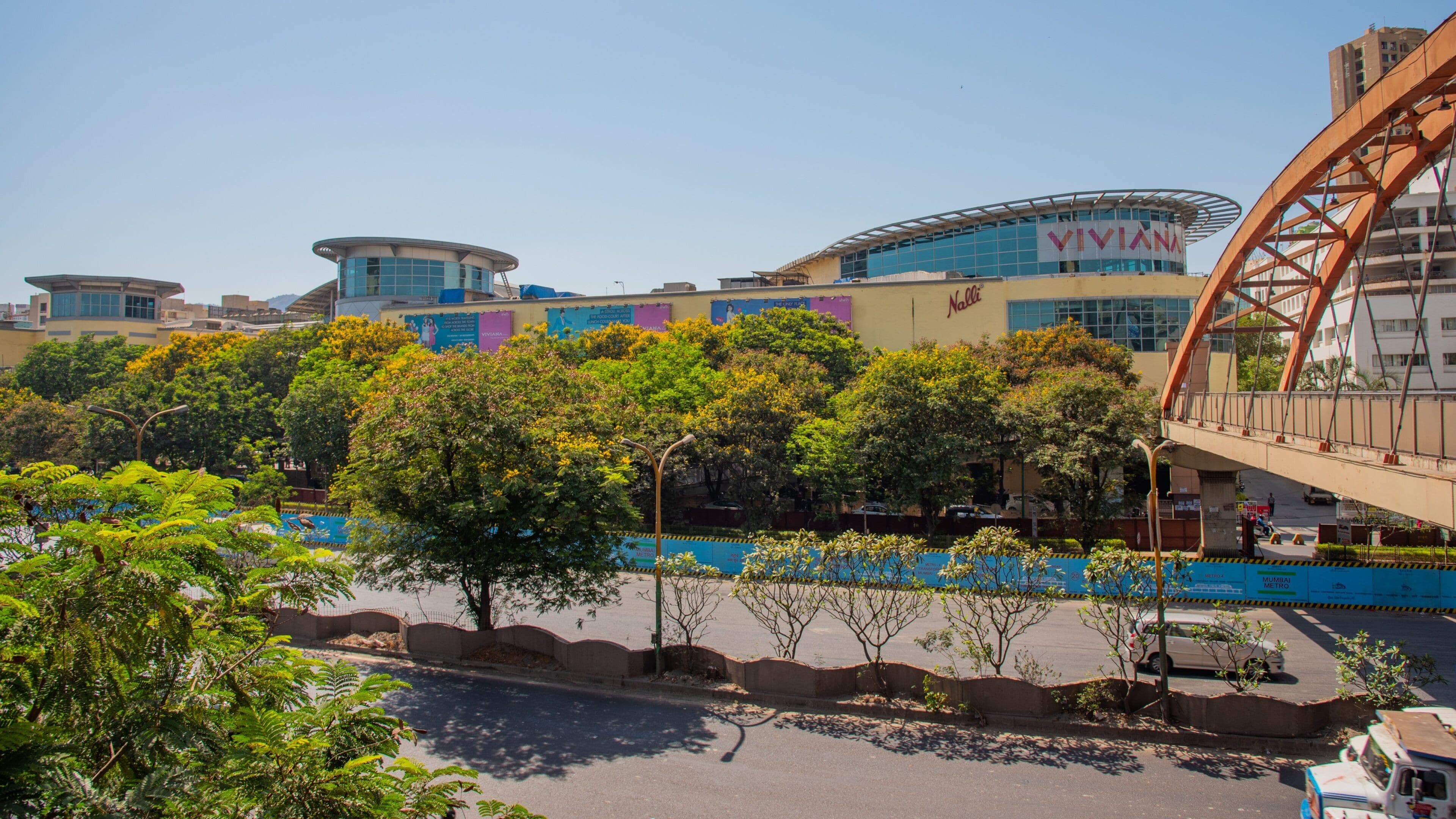 A modern urban area with a large shopping mall, a bridge, and lush green trees.
