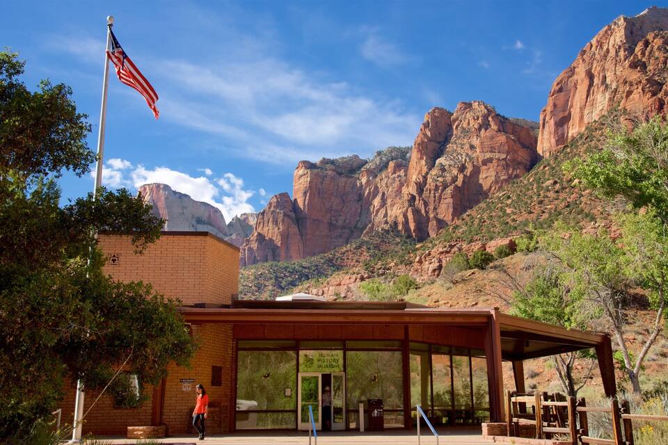 A brick building with a glass entrance, an American flag, and a mountainous backdrop.