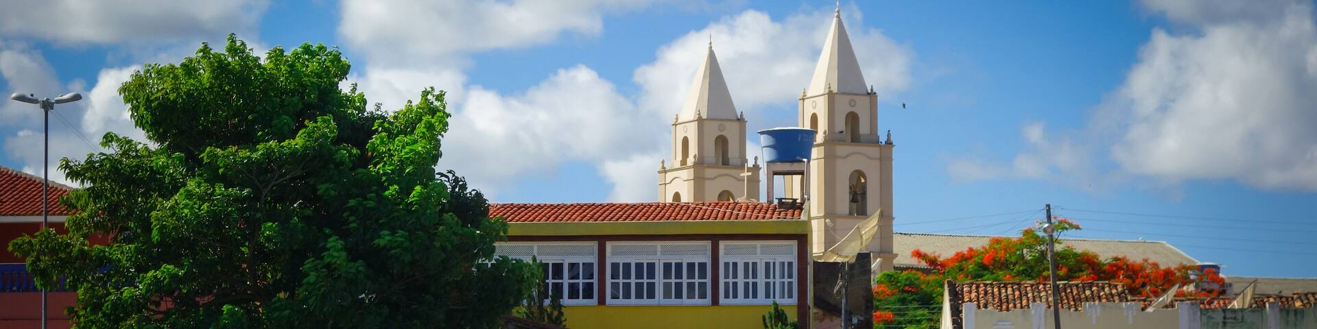 Piacabucu/Alagoas/Brazil: men seated under the shadow of a tree, houses, church and a boat on the river