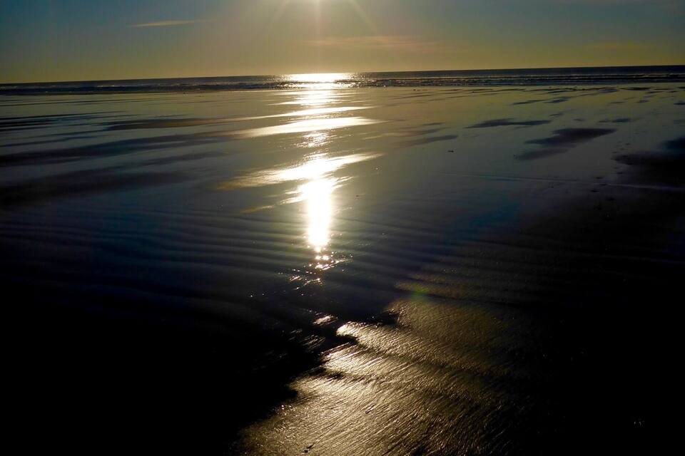 Le soleil se reflète sur une plage mouillée, sous un ciel dégagé.