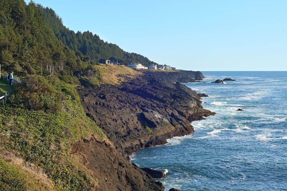 A coastal landscape with a rocky cliff, ocean waves, and a fenced path.