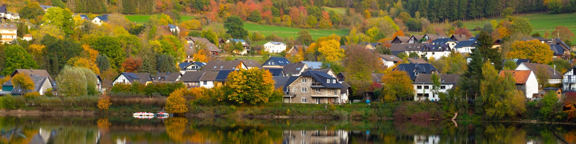 Beautiful german village with colorful foliage forest in the background and reflection in the Rursee lake, Einruhr, Simmerath