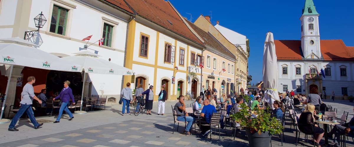 A bustling square with cafes, people walking, and historic buildings with a church tower.