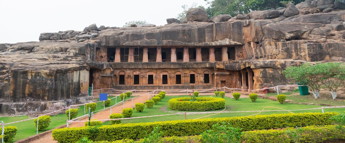 A large rock structure with carved columns and a surrounding garden.