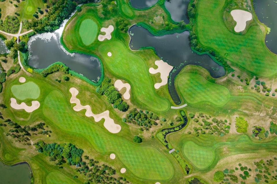 An aerial view of a golf course with multiple water hazards, sand bunkers, and lush green fairways.