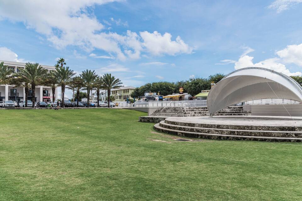 Un parque con un anfiteatro circular, palmeras y un edificio con un letrero.