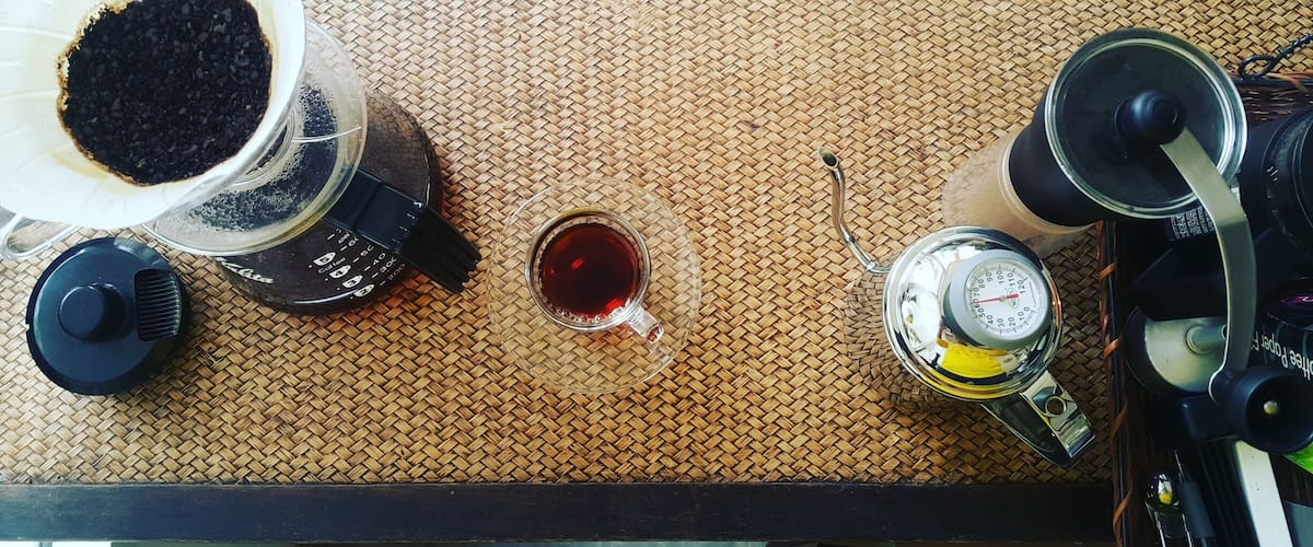 A coffee maker, a scale, and a cup of coffee on a woven tray.