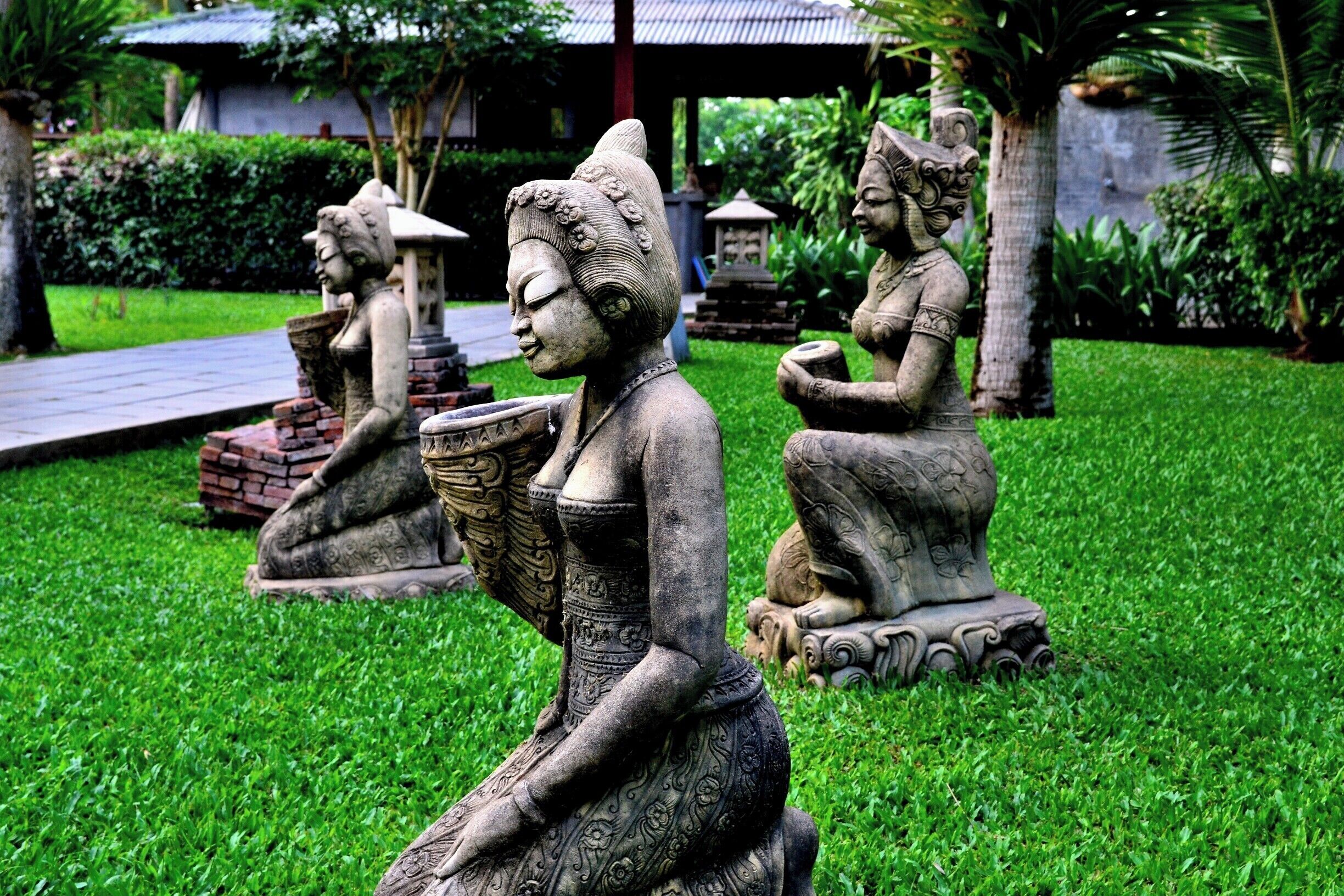 Three stone statues of women in traditional attire sitting on grass.