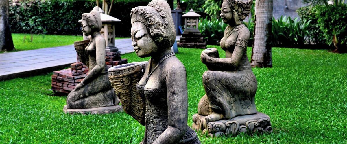 Three stone statues of women in traditional attire sitting on grass.