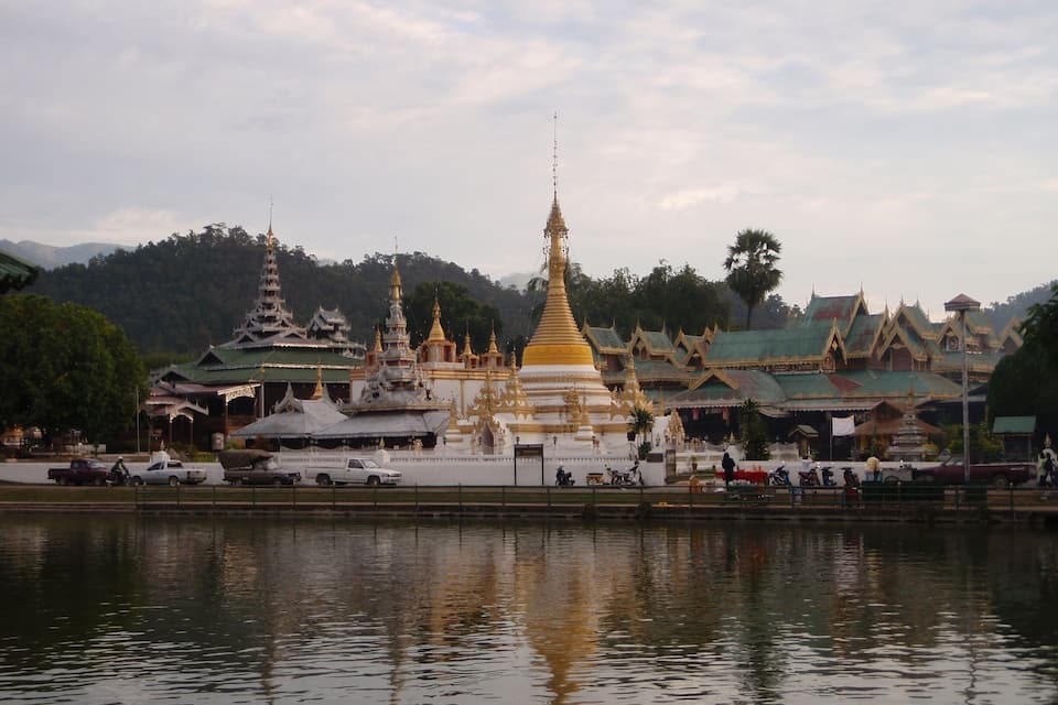 A temple complex with multiple golden spires and traditional architecture by a calm body of water.
