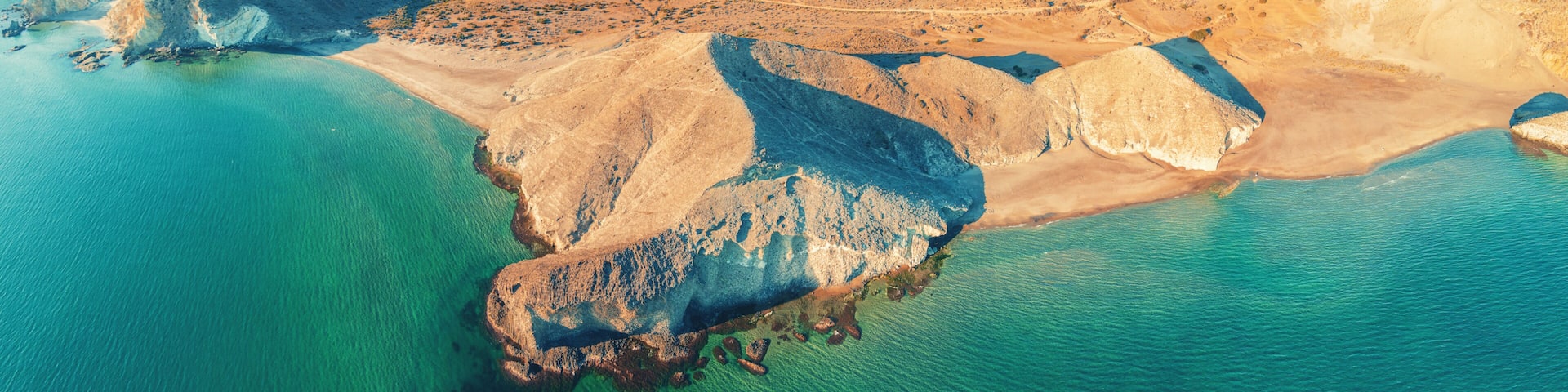 A coastal landscape with a prominent rocky outcrop surrounded by turquoise waters.