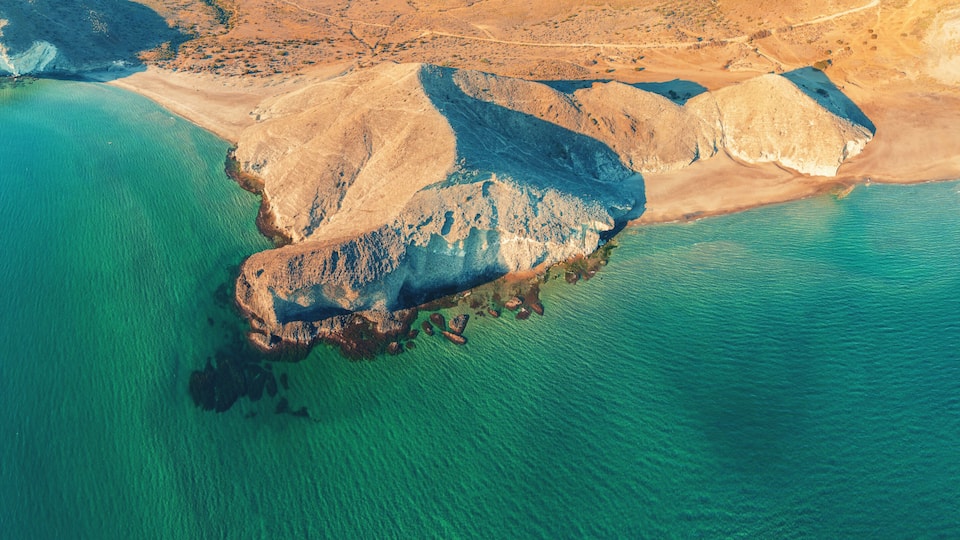 A coastal landscape with a prominent rocky outcrop surrounded by turquoise waters.