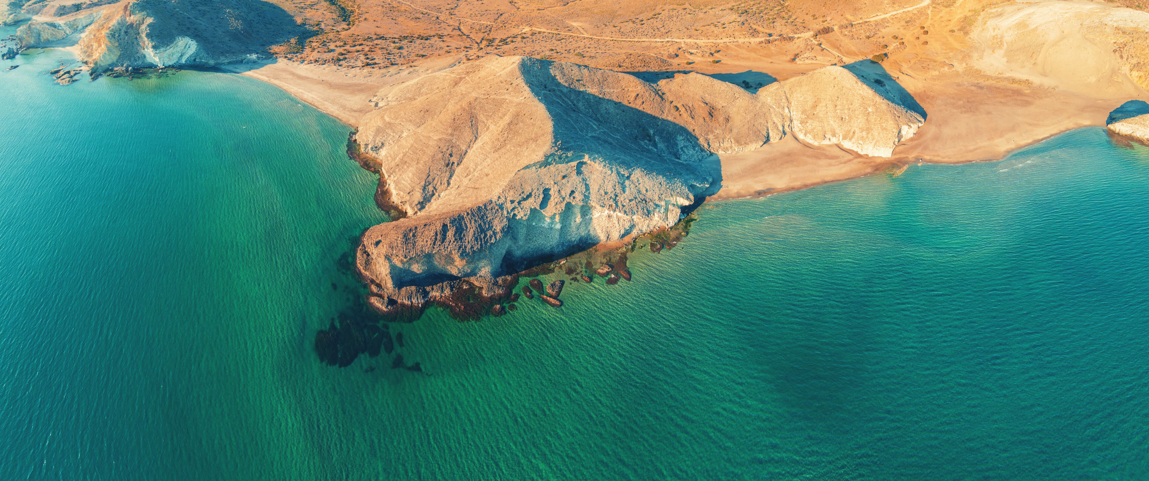 A coastal landscape with a prominent rocky outcrop surrounded by turquoise waters.