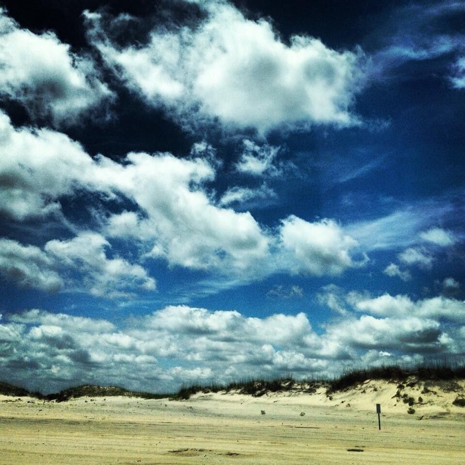 A beach with sand dunes and a partly cloudy sky.