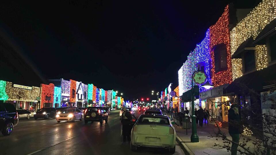 A street lined with brightly lit buildings and cars parked along the road.